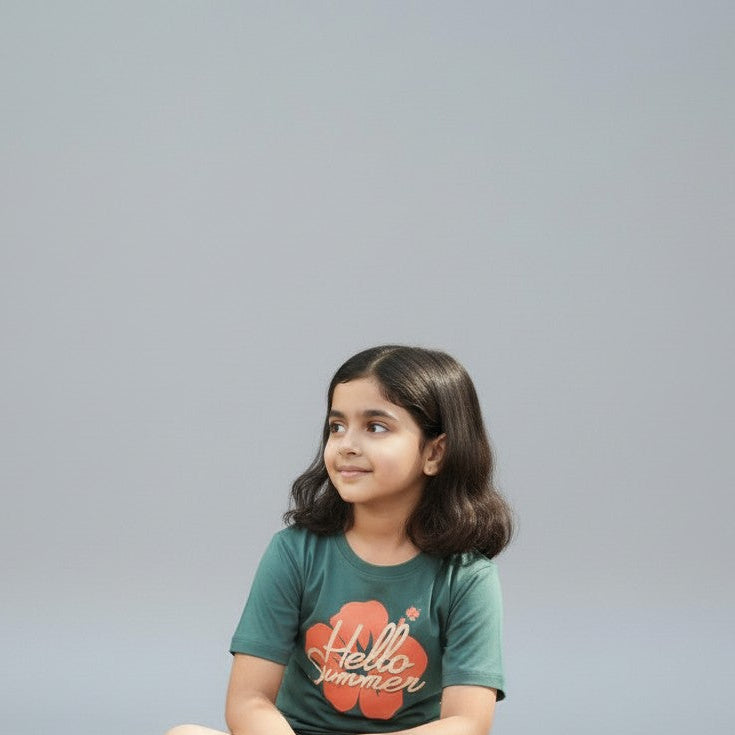 Young girl sitting on a light gray floor wearing a green t-shirt with 'Hello World' printed on it.